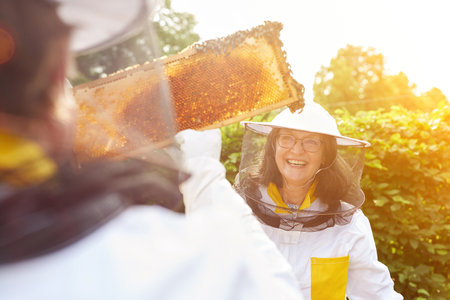 Happy female beekeeper and man holding honeycomb frame in gardenの写真素材