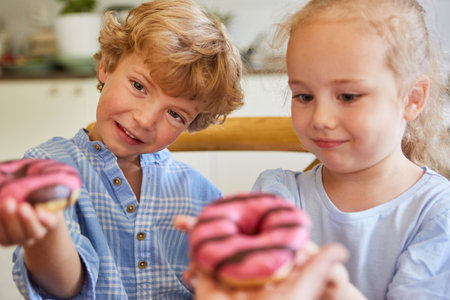 Curious siblings examining fresh donuts in kitchen at homeの写真素材