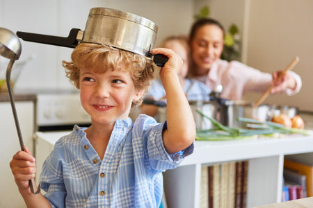 Cute boy playing with cooking pot and ladle in kitchen at homeの写真素材