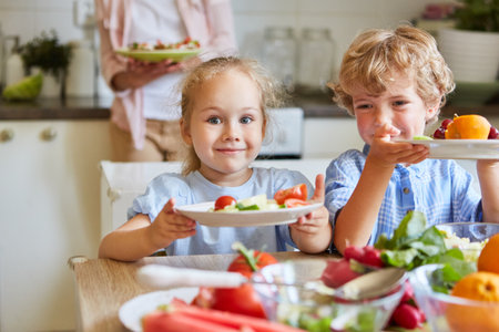 Portrait of smiling girl sitting with brother holding fruit plate in kitchen at homeの写真素材