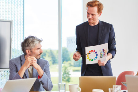 Confident businessman showing chart to male colleague in officeの写真素材