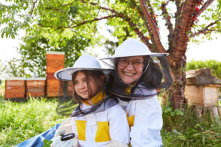 Portrait of smiling senior female beekeeper with girl holding magnifying glass in apiary gardenの写真素材