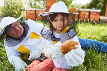Girl looking at beeswax near senior male beekeeper in apiary garden during summer