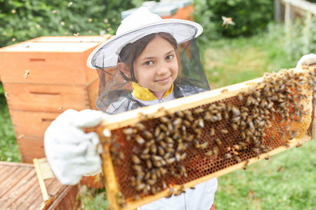 Portrait of girl holding beeswax frame with honey bees while standing at apiary garden