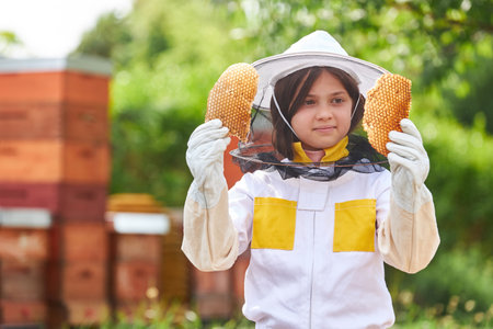 Girl examining organic beeswax wearing protective suit at apiary garden in summerの写真素材
