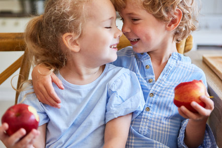 Happy siblings enjoying with each other holding apples at homeの写真素材