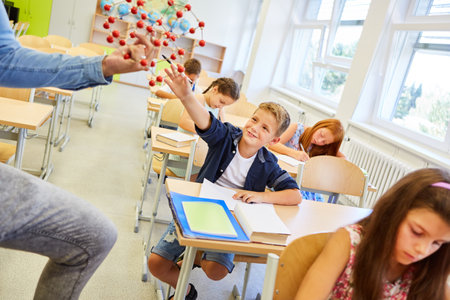 Smiling schoolkid touching molecular structure sitting on bench in classroomの写真素材