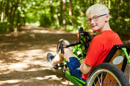 Portrait of smiling blond boy with disability sitting on recumbent bike at forestの写真素材