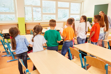 Rear view of male and female students standing side by side with teacher during activity in classの写真素材