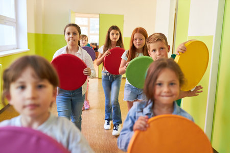 Group of children holding colorful cushions while walking in hallway at schoolの写真素材