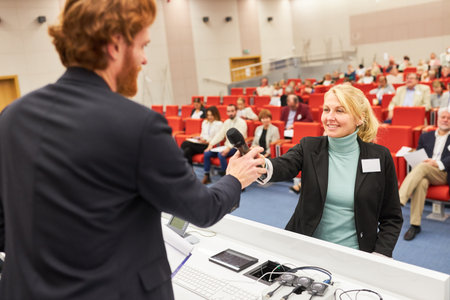 Speaker giving microphone to woman in audience during business event in auditorium