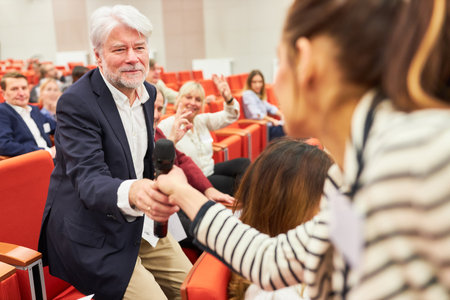 Businesswoman giving microphone to male audience during business seminar in auditorium