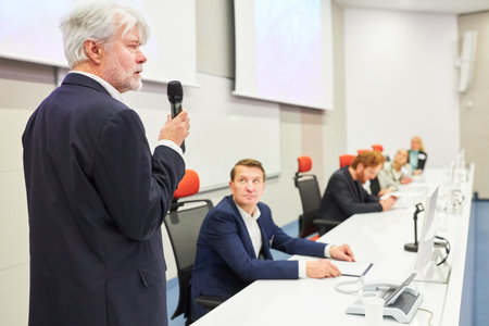 Speaker explaining while standing by professionals on stage in convention centerの写真素材