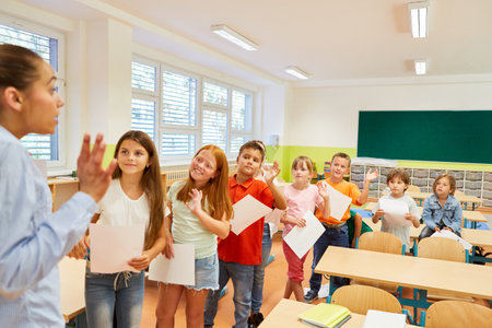 Group of elementary school children waving at female teacher in classroom