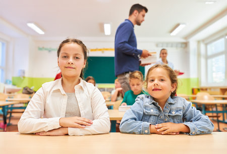 Portrait of elementary schoolgirls sitting together on bench in classroom at schoolの写真素材
