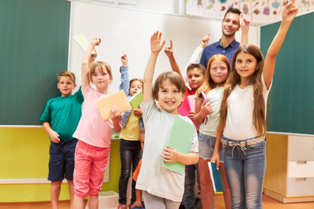 Group of happy school kids raising hands in classroomの写真素材