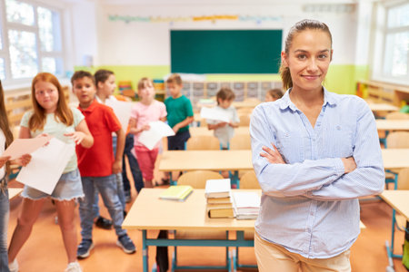 Portrait of smiling female elementary teacher standing with arms crossed in classroomの写真素材