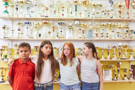 Male and female school students standing with arms around in front of trophies on display shelf at schoolの写真素材