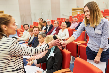 Female professional giving microphone to businesswoman during business conference in auditorium