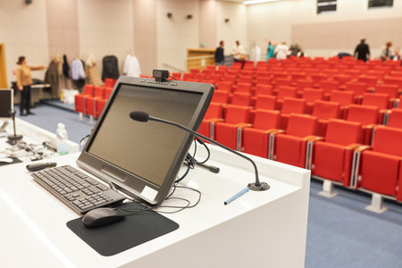 Microphone by computer at podium in front of red chairs at business conference