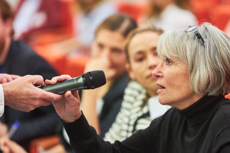 Businesswoman answering through microphone during business session in convention centerの写真素材
