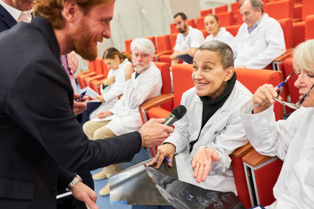 Male speaker asking smiling female doctor in audience of conference in convention center