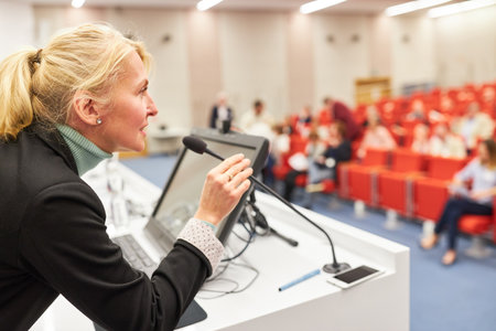 Female speaker at business conference discussing with audience through microphoneの写真素材