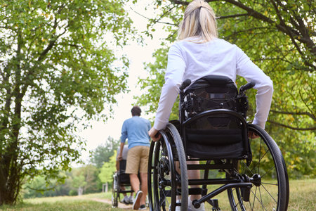 Two individuals who use wheelchairs are spending time outdoors surrounded by greenery, signifying inclusion andの写真素材