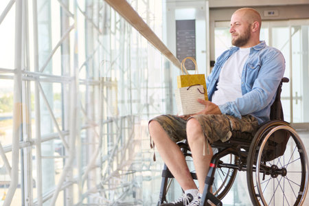 Person with lower limb impairment in a wheelchair holding a gift bag, symbolizing accessibility and...