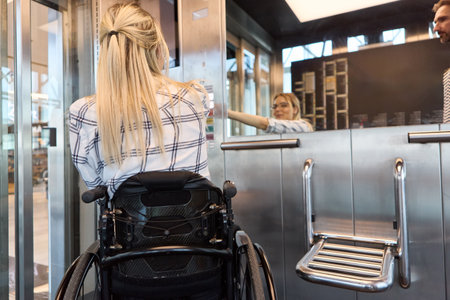 Back view of a person in a wheelchair at a service counter interacting with an employee, showing inclusion and accessibility.の写真素材