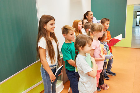 Group of smiling male and female students standing together holding books in classroom
