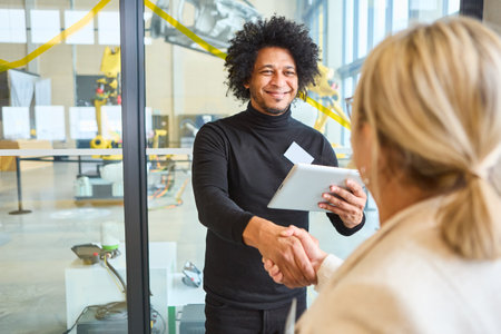 A friendly business meeting in a robotics lab featuring a handshake and smile, highlighting collaboration in technology and robotics.の写真素材