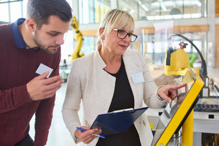 Two engineers reviewing an automation process in a robotics lab using a touchscreen interface. The...
