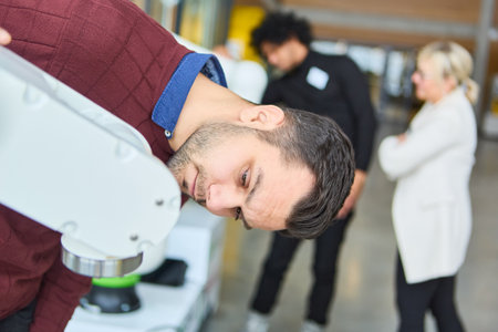 Engineer closely examines a robot gripper arm during a hands-on robotics training session, with...