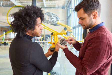 Two engineers analyzing a robotic arm part in a modern industrial setting, focusing on automation, technology, and innovation in manufacturing.の写真素材