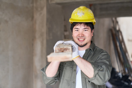 Smiling male carpenter carrying planks on shoulderの写真素材