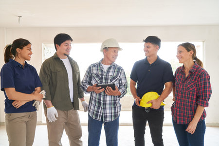 Smiling contractor holding tablet PC discussing with teamの写真素材