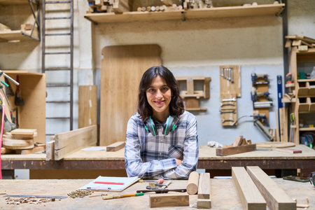 A young carpenter smiles confidently while surrounded by wooden materials in a busy workshop. The...