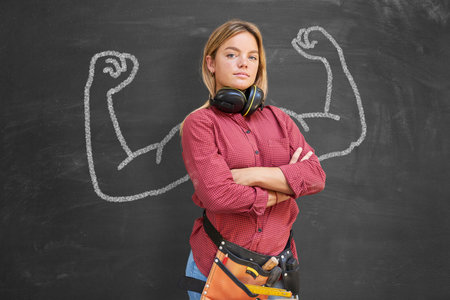 Young woman as a craftswoman in front of a blackboard with muscular arms as a career concept