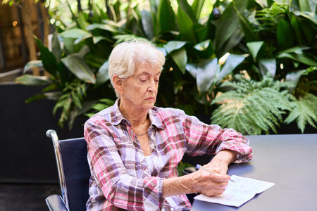 Elderly woman seated at a table, focusing on a cognitive task in a serene environment.の写真素材