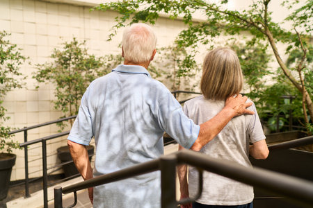 An elderly man and woman walking near garden greenery, symbolizing support and recovery. The serene environment suggests a rehabilitation setting emphasizing care, companionship, and well-being for seniors.の写真素材