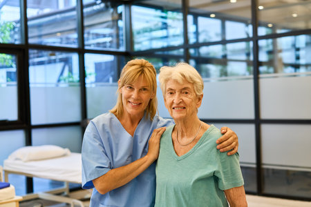 A senior woman and her caregiver smiling in a healthcare facility. Symbolizing support, rehabilitation, and care, this image captures a positive interaction between a senior resident and a healthcare provider.の写真素材