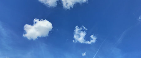 Panoramic image of a vibrant blue sky scattered with a few fluffy white clouds, ideal as a tranquil concept or scenic background. The clarity and brightness evoke freshness and a calm atmosphere.の写真素材