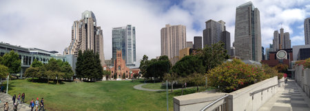 A wide panoramic view of an urban park surrounded by towering skyscrapers under clear skies.の写真素材