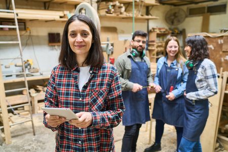 A group of diverse people collaborating in a woodworking shop, showing teamwork and apprenticeship. An older woman supervises, highlighting the training environment.の写真素材