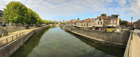 Panoramic view of a charming town by the river featuring historic buildings, lush trees, and a sunny atmosphere, capturing the essence of a serene and picturesque day by the water.の写真素材
