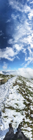A breathtaking panoramic view of a snow-covered mountain trail beneath an expansive blue sky adorned...