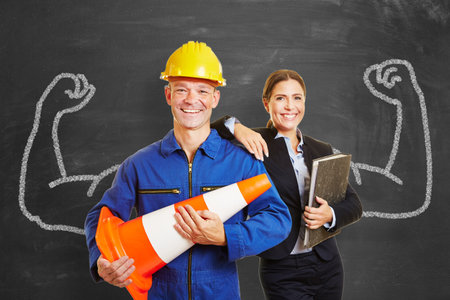 Assembler and businesswoman together as a dynamic team in front of a blackboard with muscular arms as a concept.の写真素材