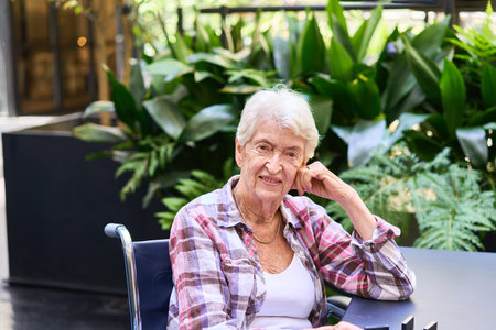 A senior woman sitting and smiling in an outdoor garden area with greenery and natural elements,...