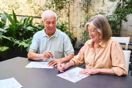 A happy senior man and woman engage in mentally stimulating activities, strengthening cognitive abilities and fostering companionship outside in a serene garden setting, promoting their mental retention and rehabilitation.の写真素材